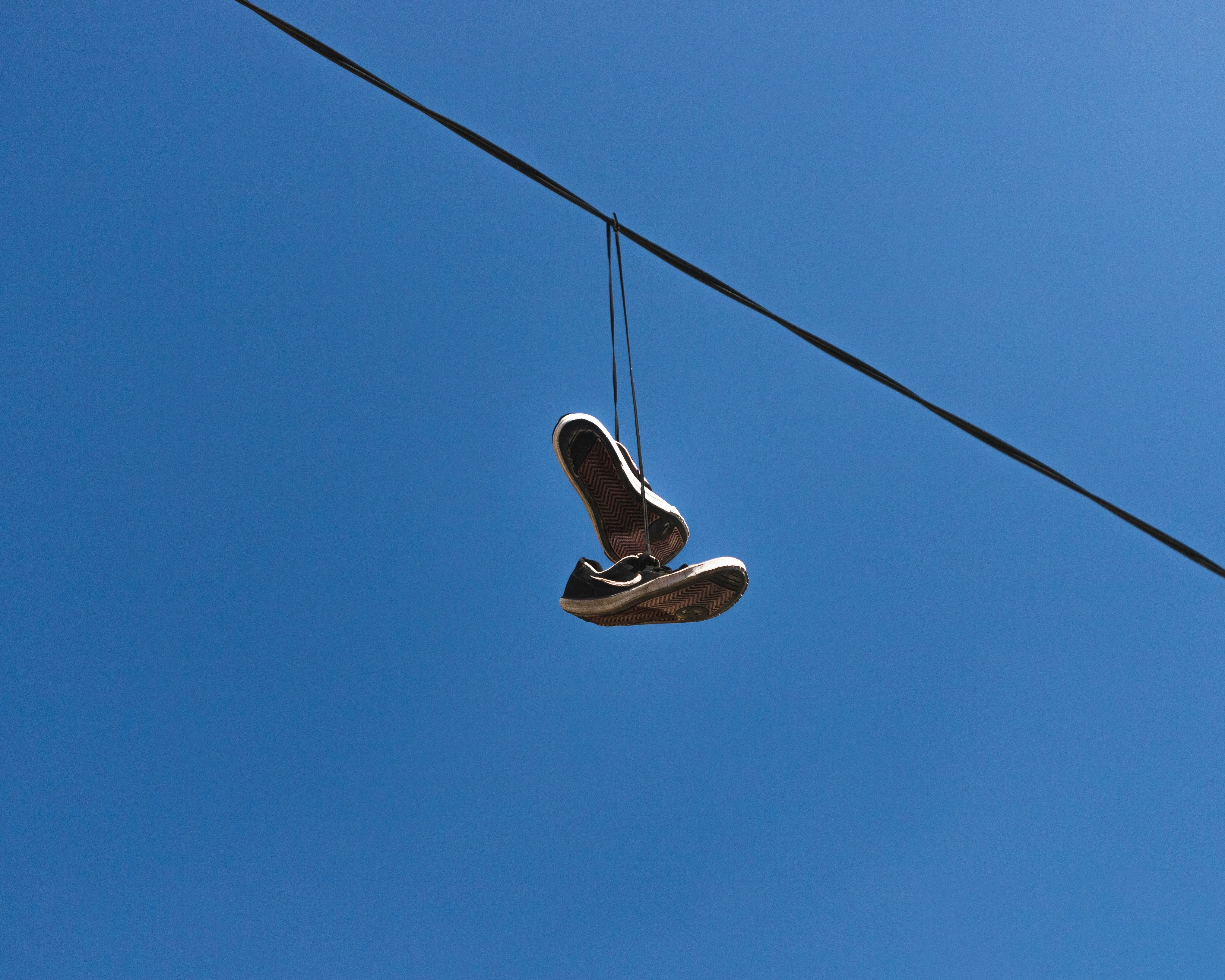 black and white sneakers on black wire under blue sky during daytime